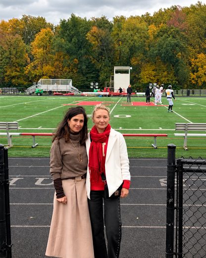 The two of us on an autumn afternoon by a sports field, one in a long beige skirt, the other in a white jacket and red scarf.